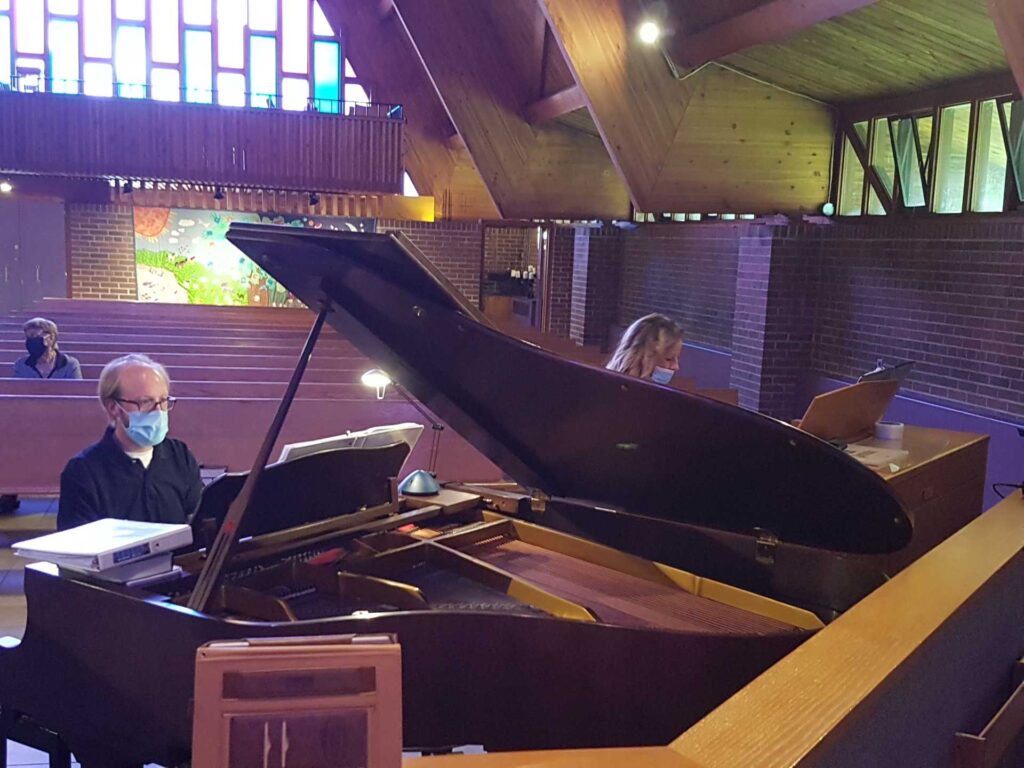 Woman at at organ next to man at a grand piano playing a duet in a church at a service