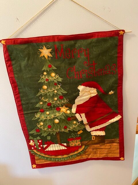 fabric wall-hanging depicting Santa Claus next to a Christmas tree