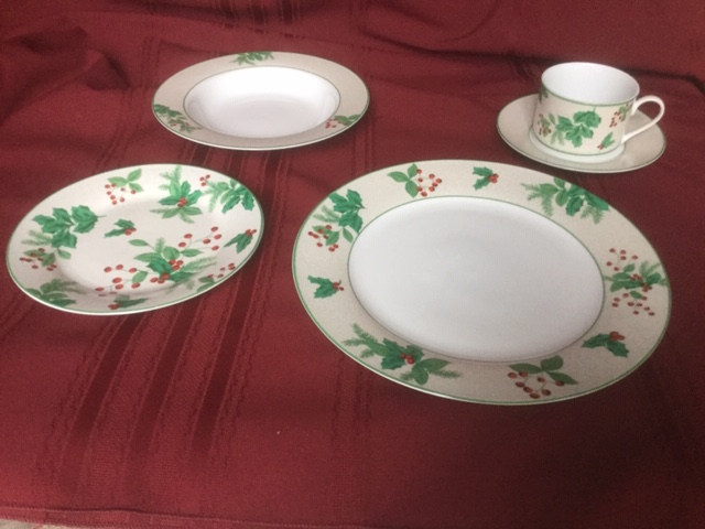 dinner plate, side plate, soup bowl, cup and saucer, each with holly and berry motif, set against a red fabric background