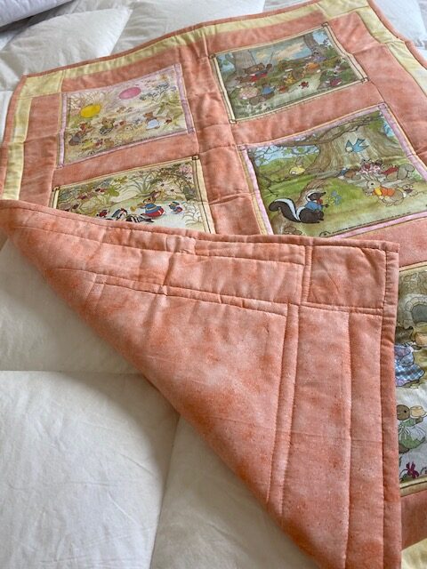 machine-quilted baby quilt with woodland creature scenes, turned up at one corner
