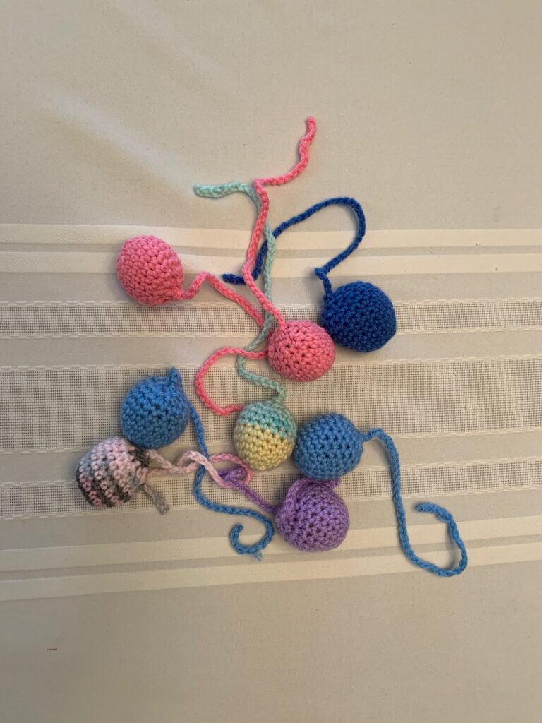 8 coloured crocheted balls on a string, each ball filled with a nylon pouch of catnip