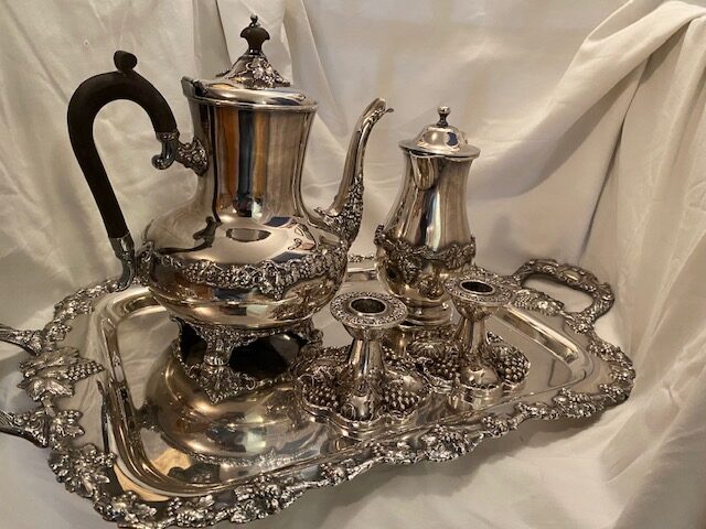 silver plate tea service with tea pot, coffee pot, and two candle sticks on a rectangular tray with two handles, all with a grape pattern