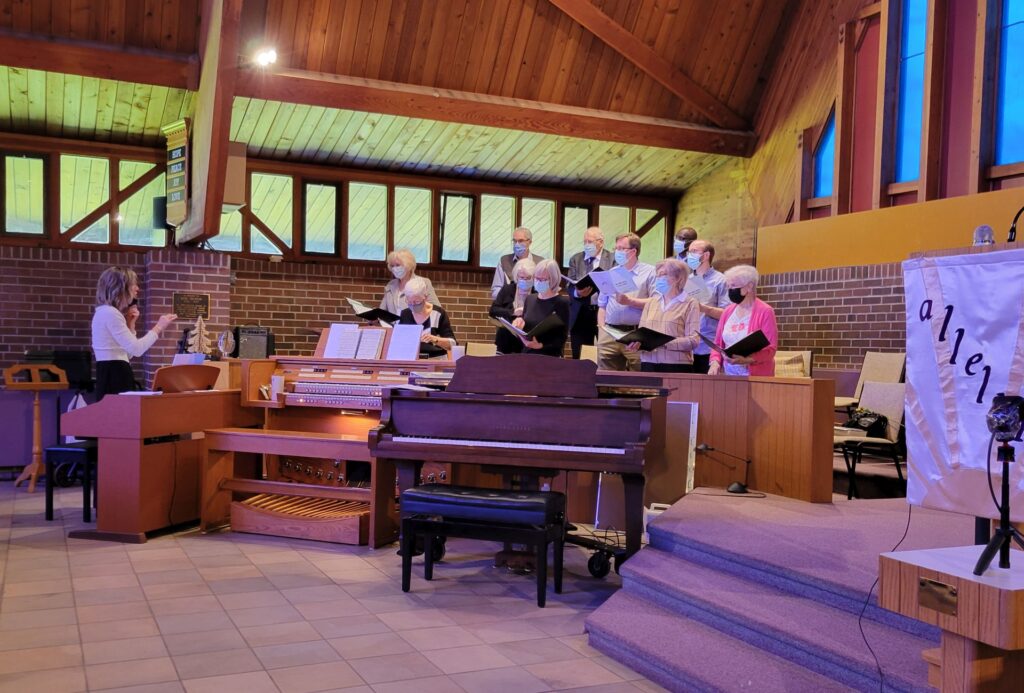 Church choir and director ready to sing, with piano, organ and keyboard in foreground